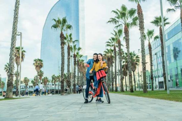 Young people making short video while riding electric bycicle in Barcelona - Happy couple having fun with new trends technology - Travel, tech and eco concept - Focus on faces