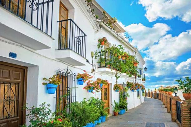 Picturesque narrow street and typical facade of white house decorated with blue flower pots in Mijas. Malaga province, Andalusia, Spain